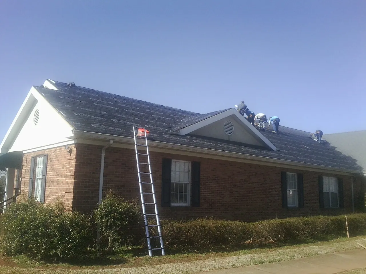 Crew tearing shingles off a brick ranch roof with a ladder set — Metal Roof Repair work by our crew in Gibsonburg