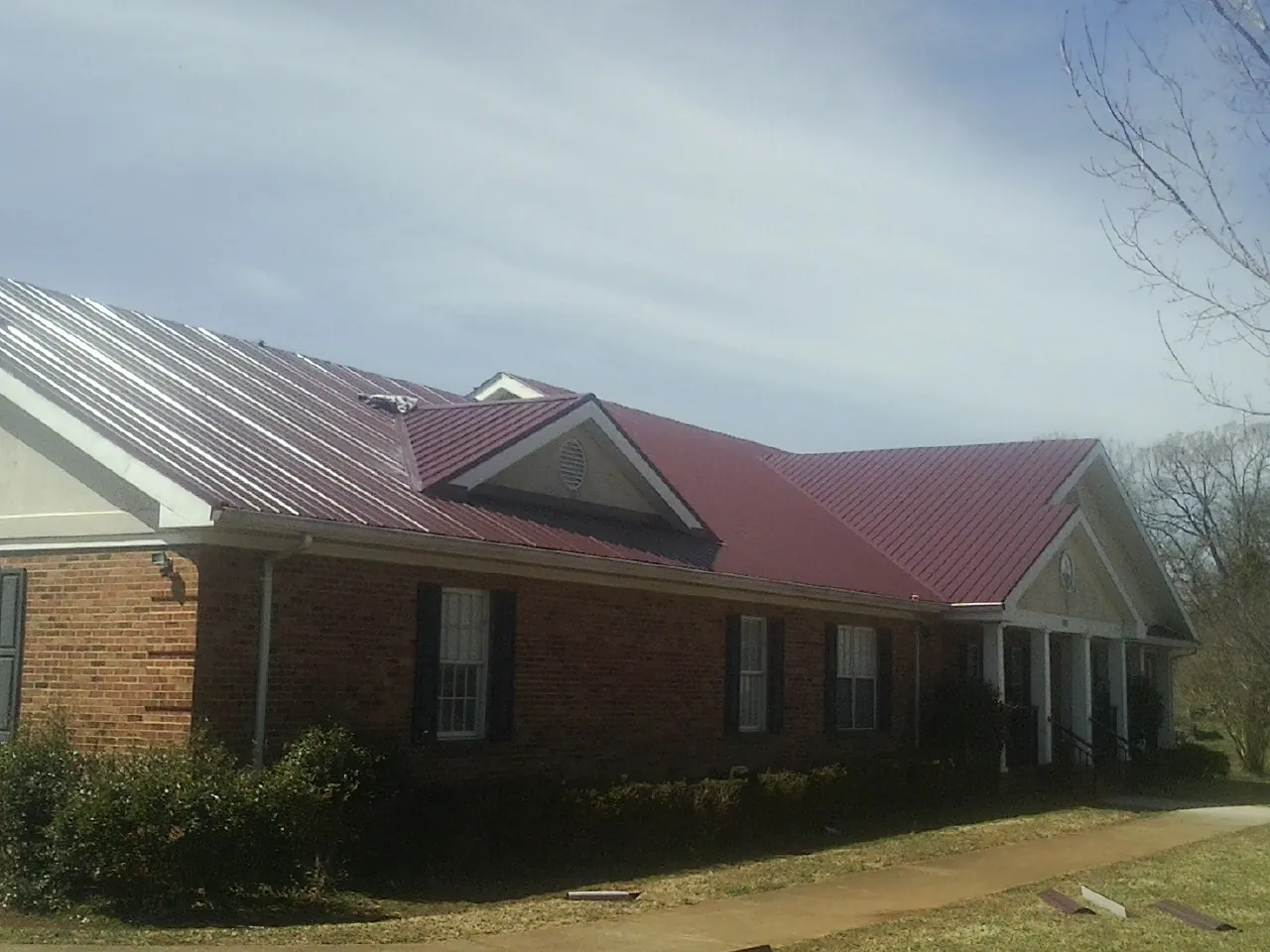 Red metal roof with gabled entries on a long brick building, from a Hail Damage Roof Repair job in Gibsonburg