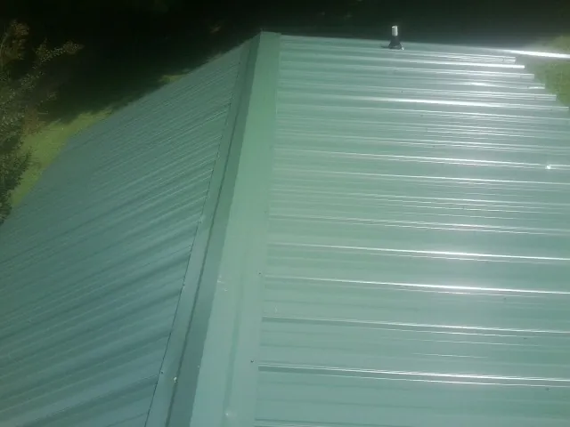 New green metal panels meeting at the ridge of a roof — Flat Roof Repair work by our crew in Gibsonburg