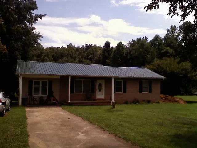 Dark green metal roof on a brick ranch with a covered porch in Gibsonburg