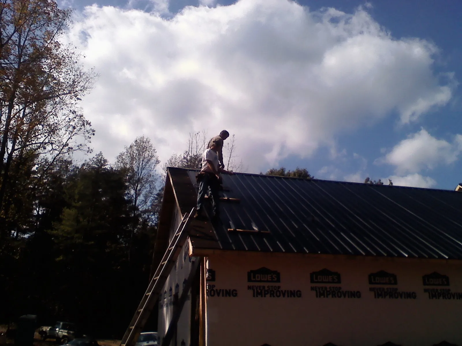 Roofer fastening dark metal panels high against a cloudy sky, from a Roof Inspection job in Gibsonburg
