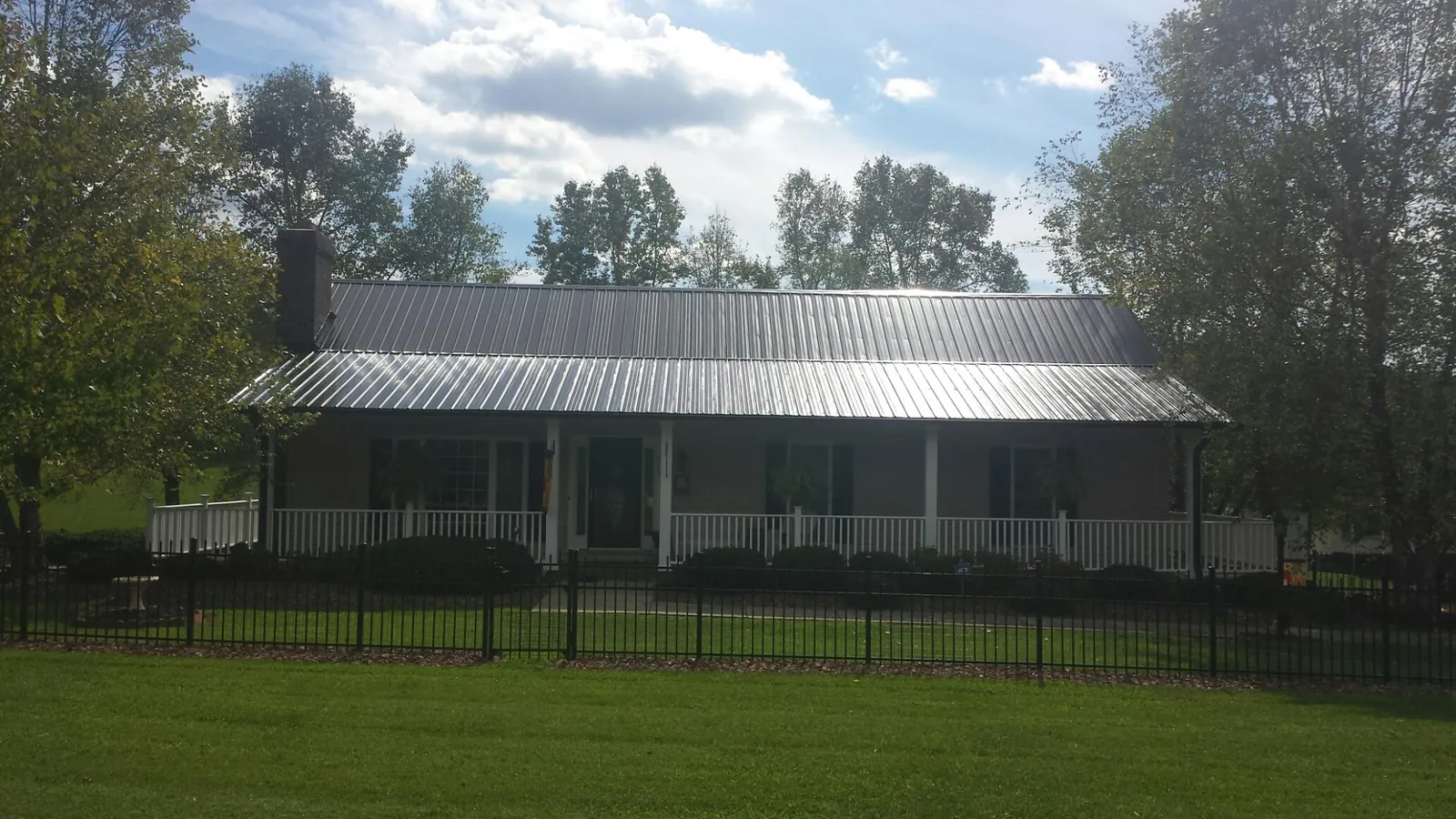 Gray metal roof on a brick ranch with a full width front porch — Gutter Guard Installation work by our crew in Gibsonburg