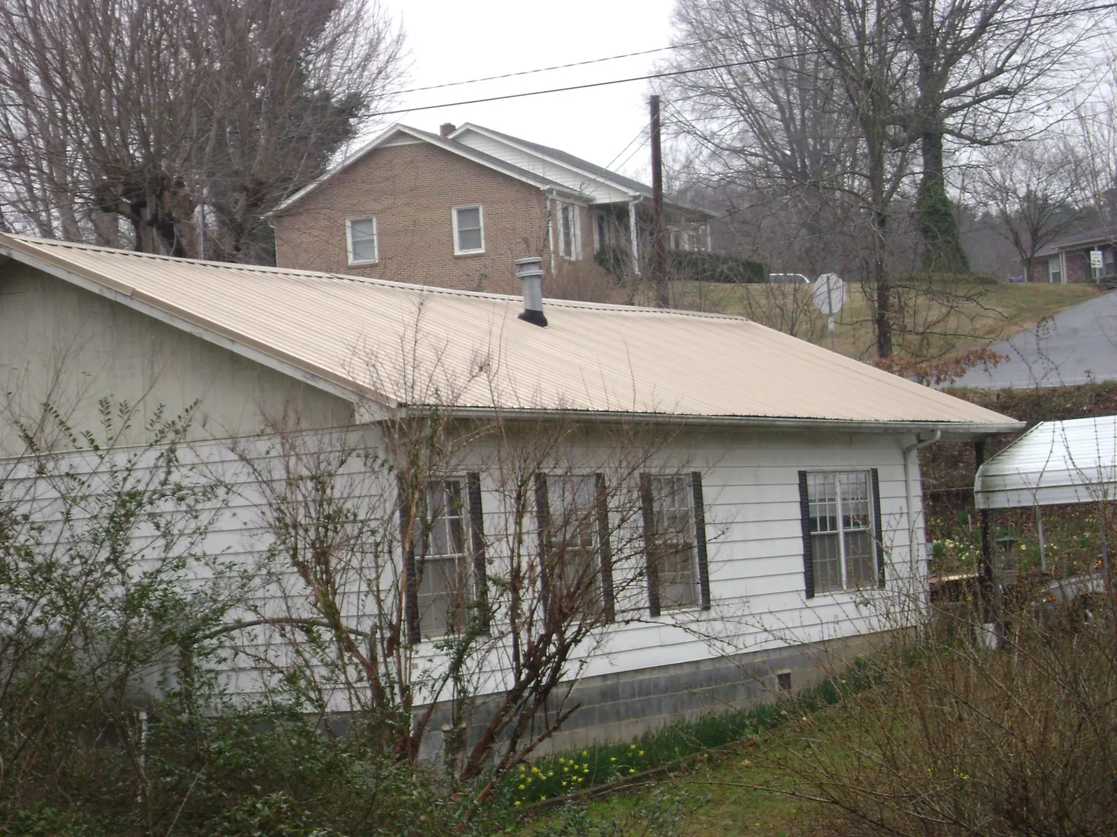 Tan metal roof on a white sided house set into a hillside — Commercial Roofing by Roofing Brothers in Gibsonburg