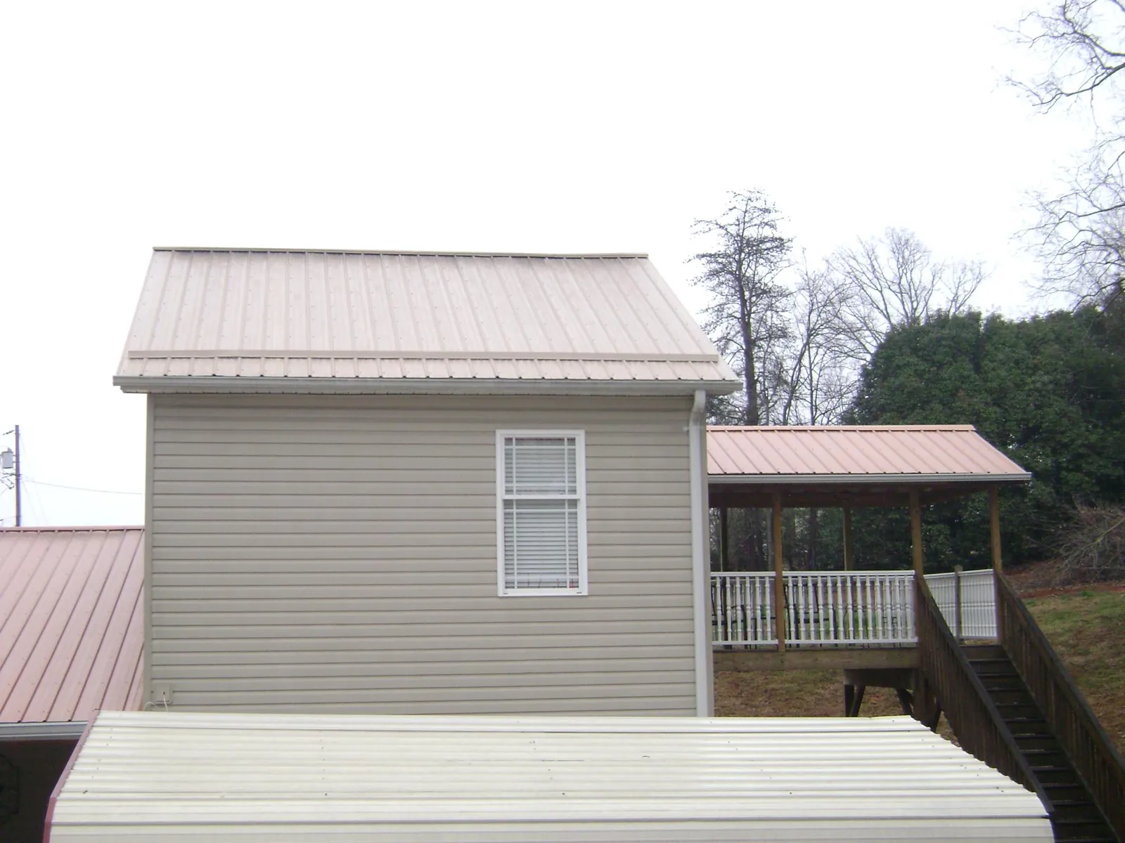 Tan metal roofs on a two story addition and attached porch, from a Roof Replacement job in Gibsonburg